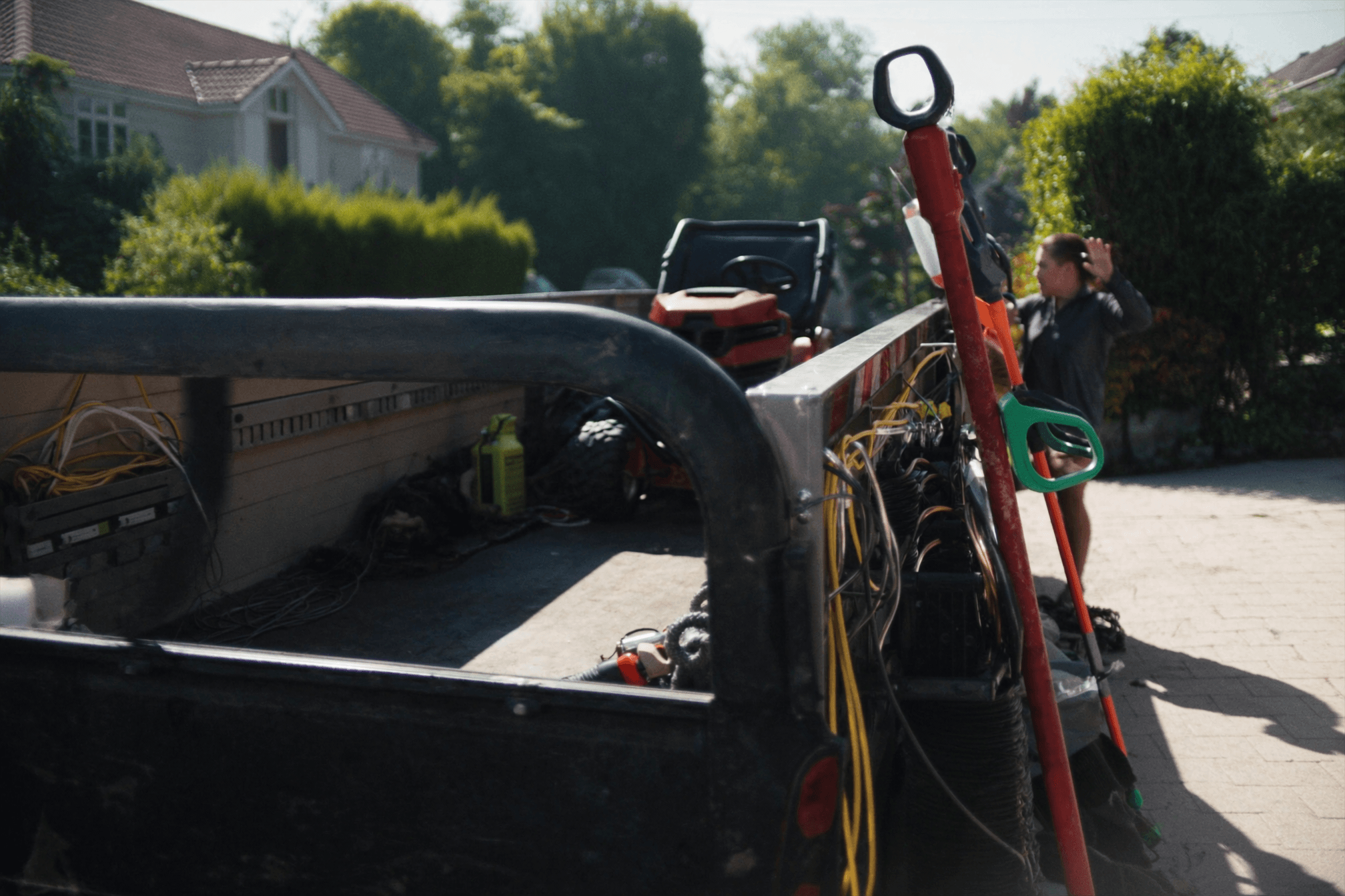 A landscaping equipment trailer loaded with mowers and trimmers, parked at the curb between jobs