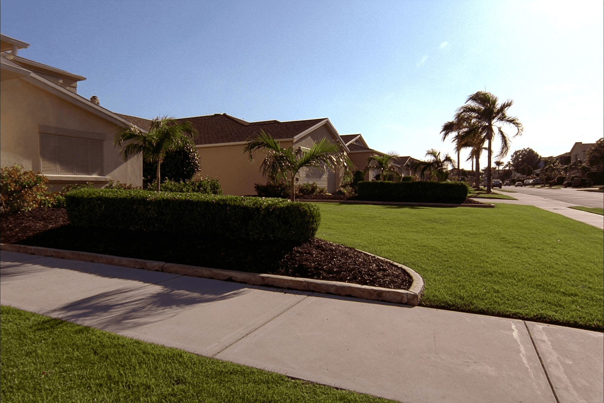 A front yard with fresh curb appeal — crisp lawn edges, mulched beds of tropical shrubs, and a tidy walkway to the door